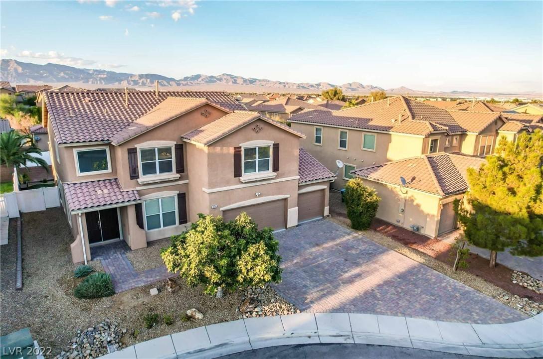 View from above a light brown stucco home with tile roofing, large garage, stone walkway, and drought friendly landscaping